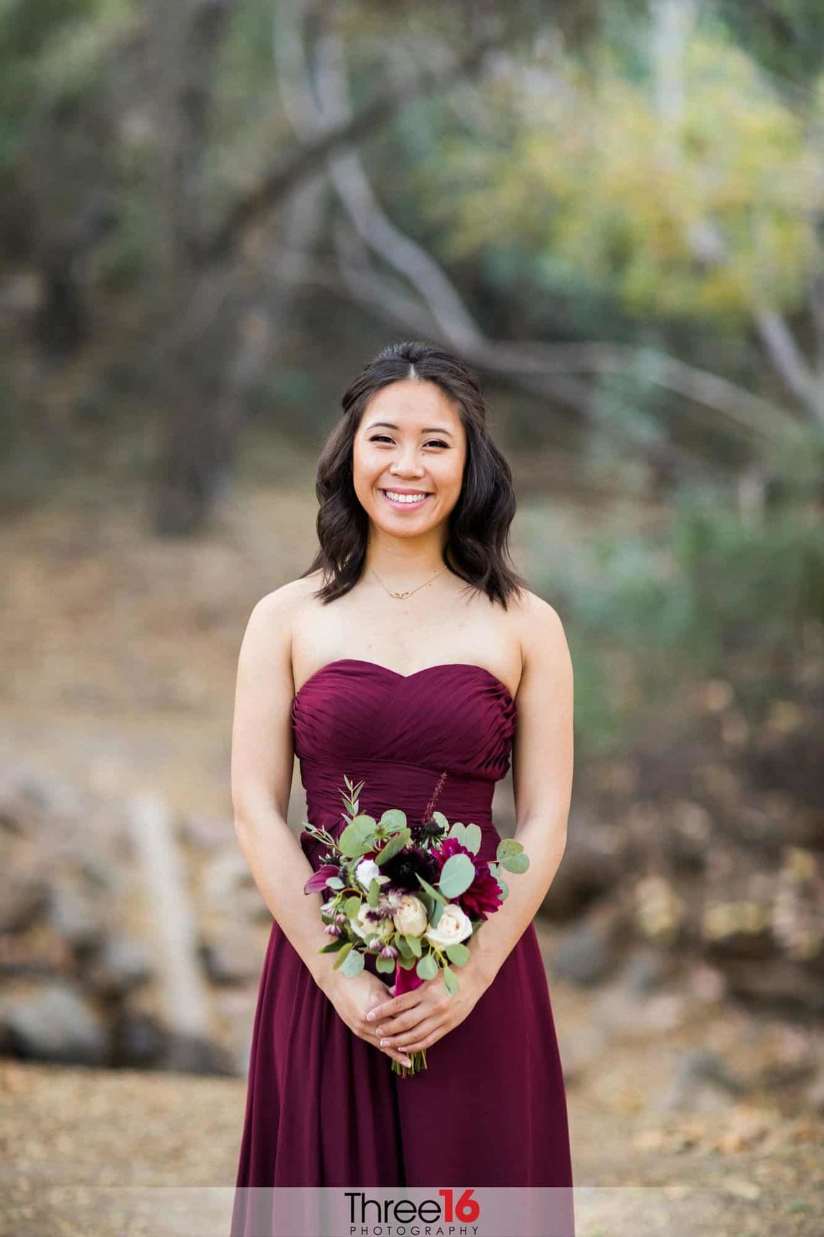 Bridesmaid poses in her burgundy dress and bouquet of flowers