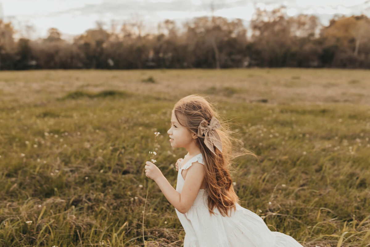 small girl blows a dandelion while in a field in pearland Texas.