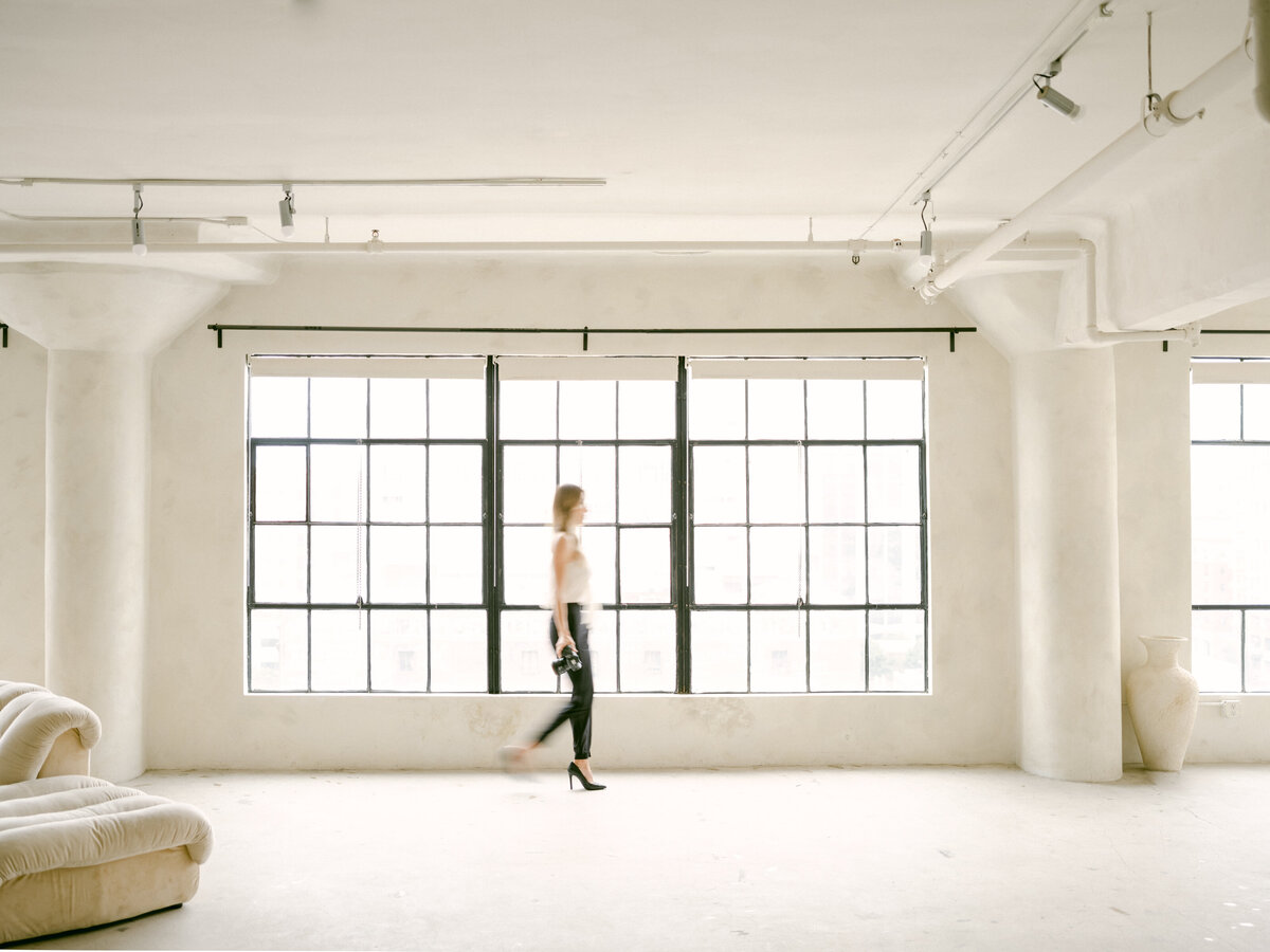 Los Angeles wedding photographer, Tiffany Gentry, walks across white studio space with black rimmed windows