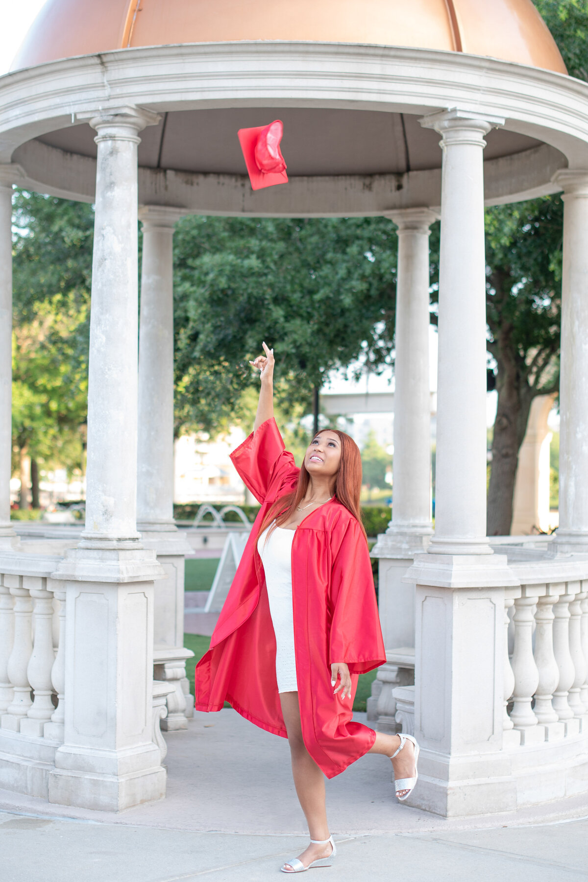 High school senior girl in gown throwing cap into the air.