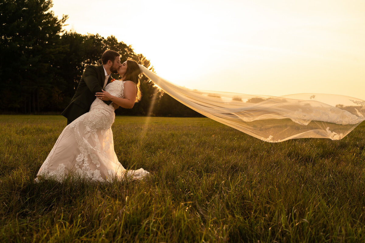Bride and groom kiss during sunset in a field.