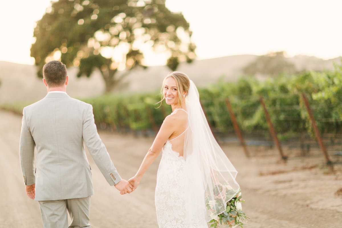 Bride and groom walk through vineyard at Firestone