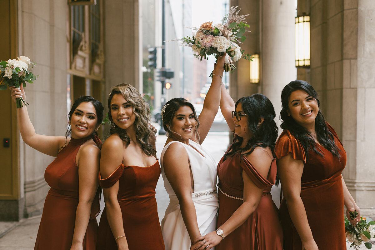 Four bridesmaids raise bouquets alongside beautiful Chicago bride after wedding ceremony.