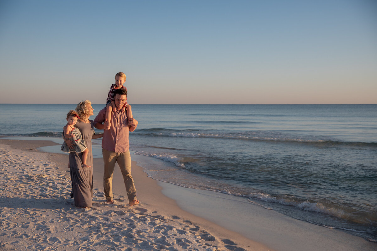 A dad with a child on his shoulder standing next to his partner holding another child