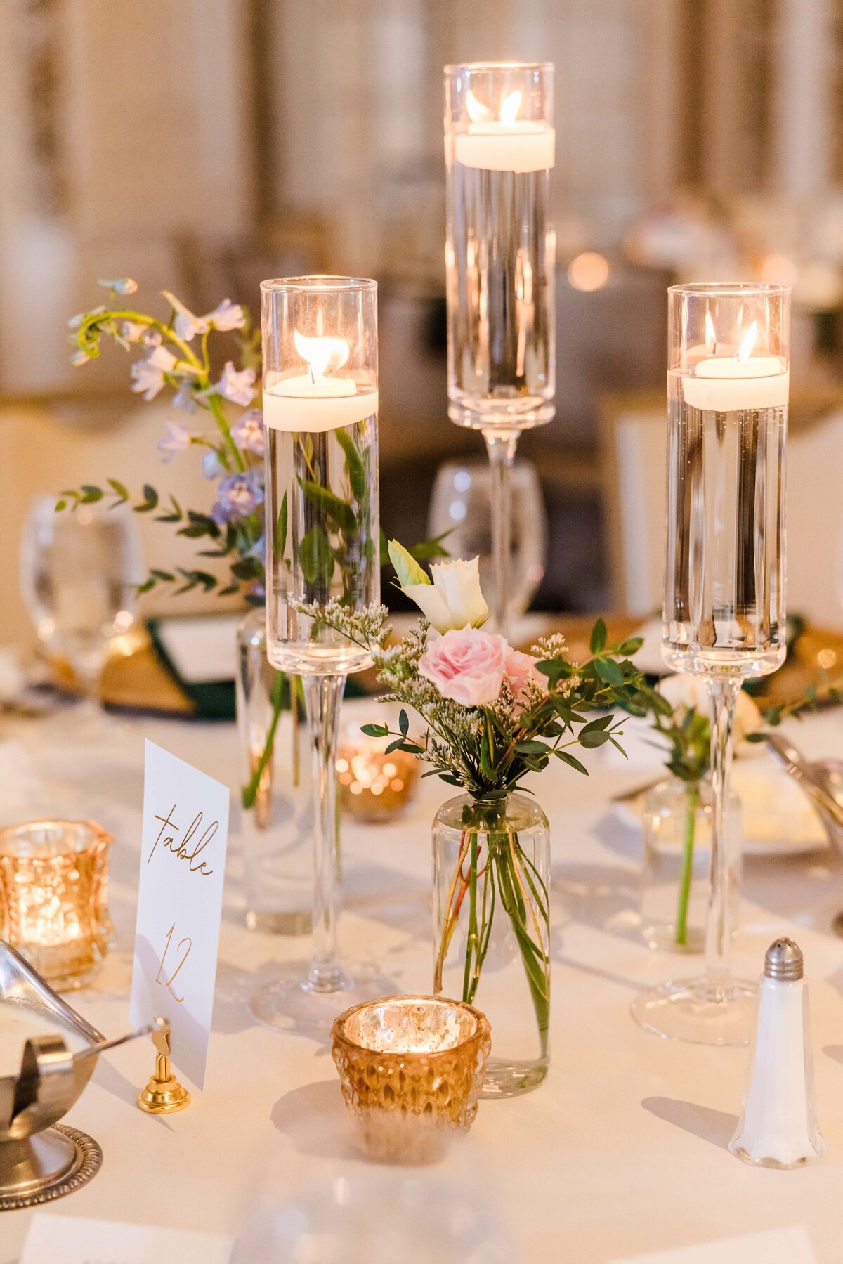 Elegant wedding table setting in Iowa featuring tall candle holders with lit candles, floral arrangements, and gold accents.