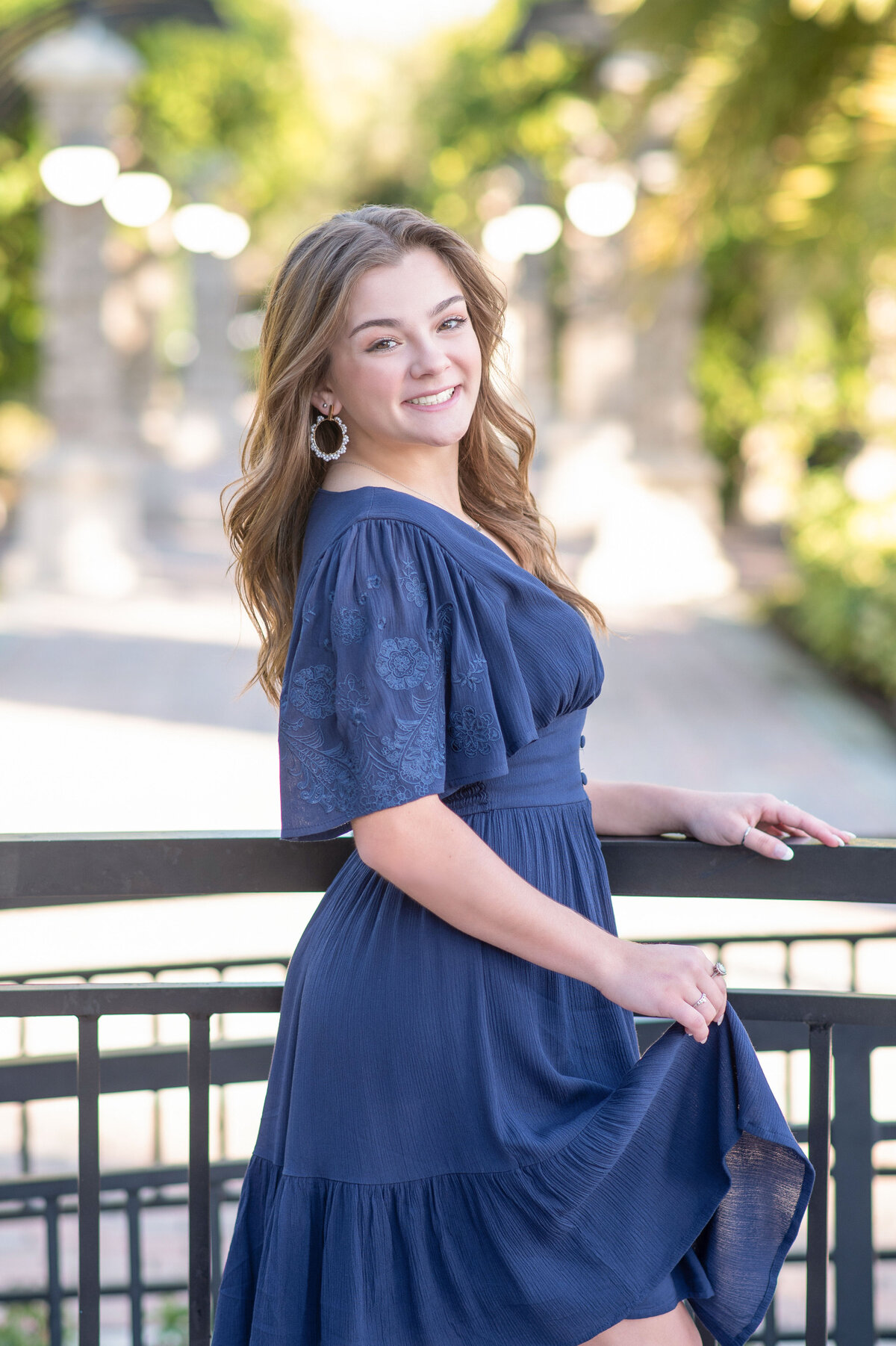 High school senior girl holding dress and railing smiles at camera.
