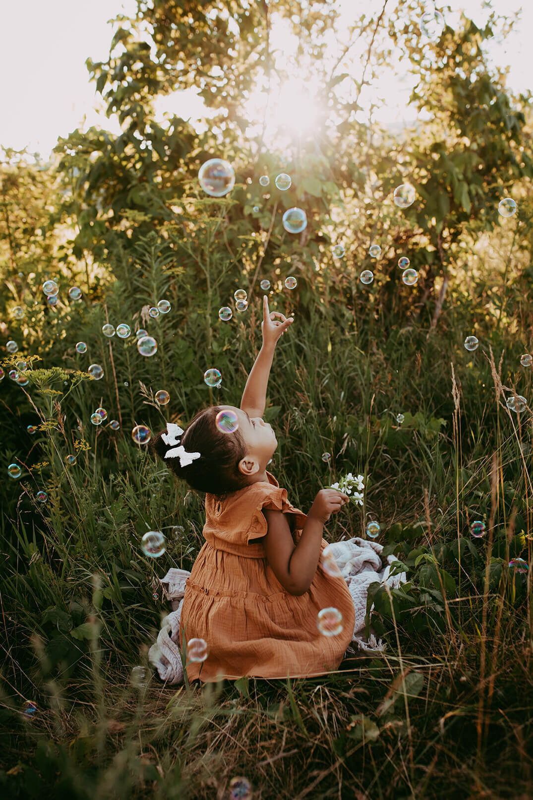 a three year old girl facing away from the camera popping bubbles in a field
