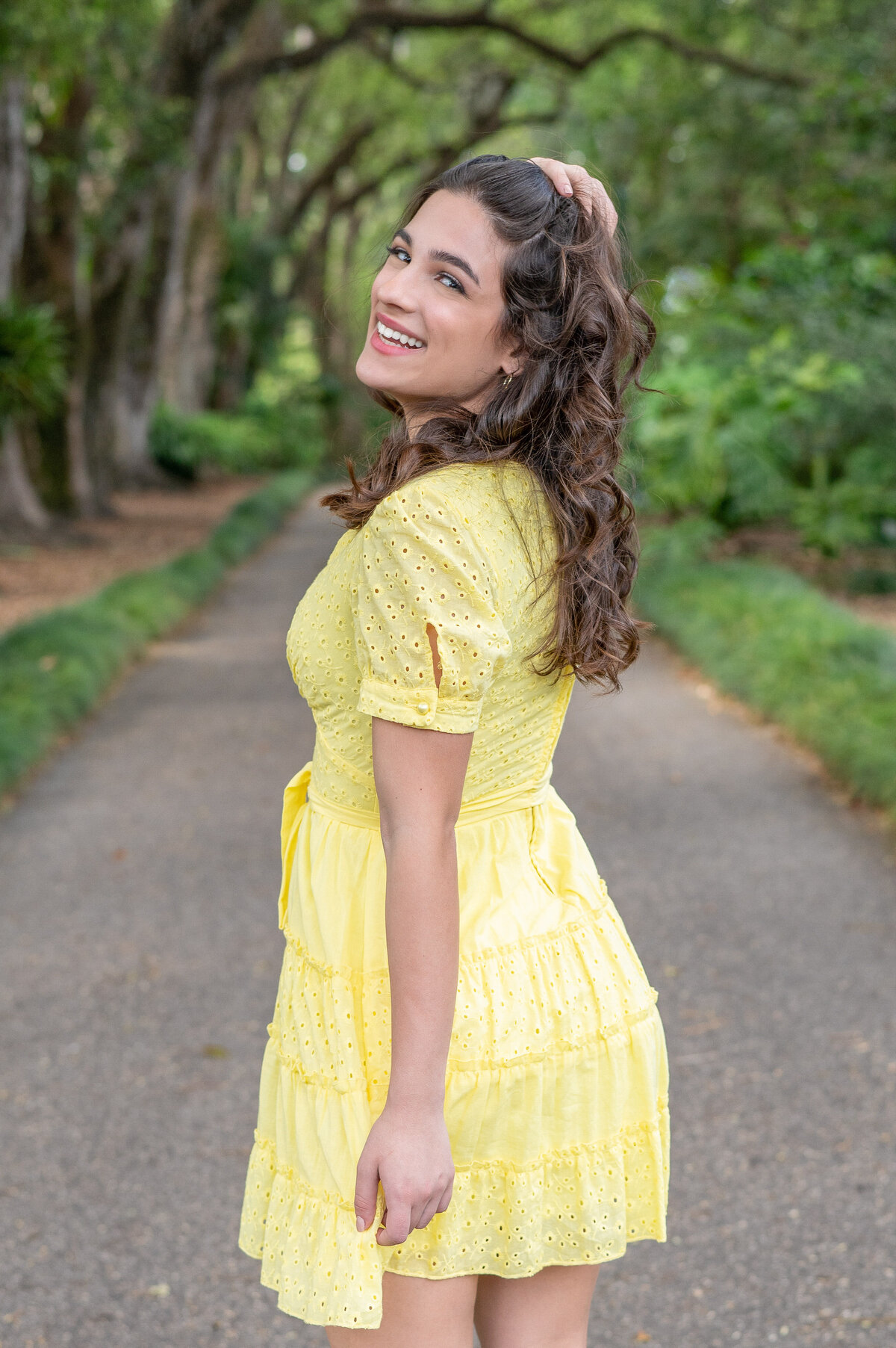 High school senior girl wearing a yellow dress with hand in her hair looks back smiling at the camera by Orlando senior Photographer Khim Higgins.