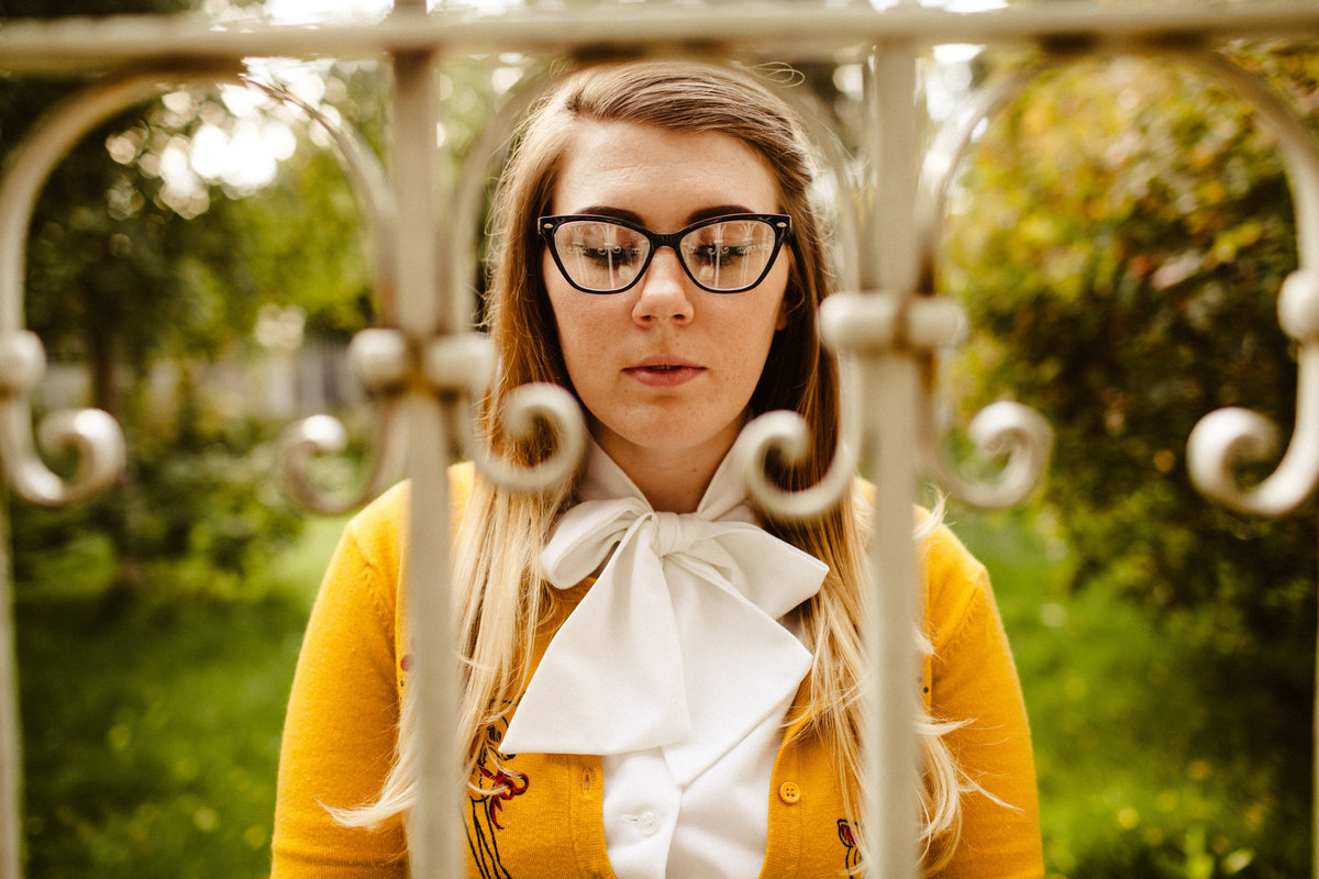 portrait of girl in retro glasses and yellow sweater through a fence