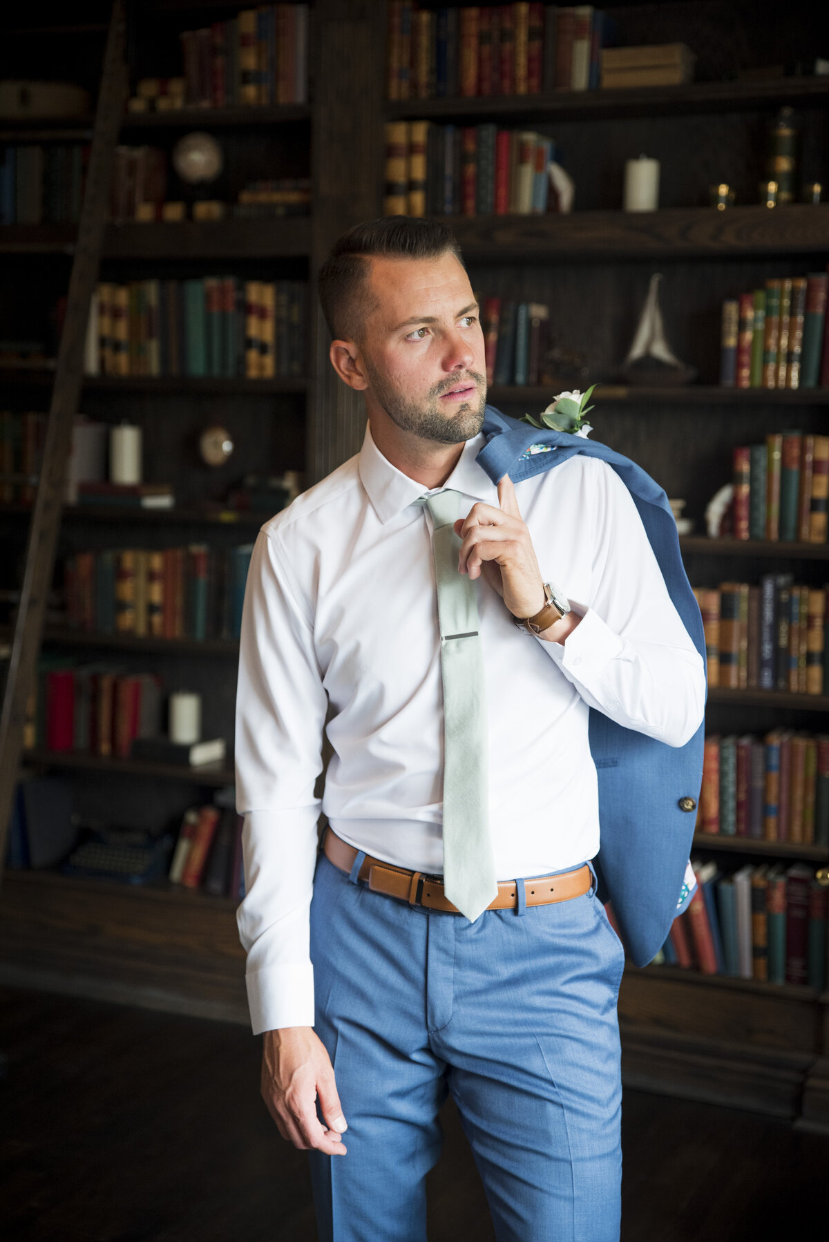 A groom looks off camera with his suit jacket draped over his shoulder in the library at The Manor House in Littleton, Colorado.