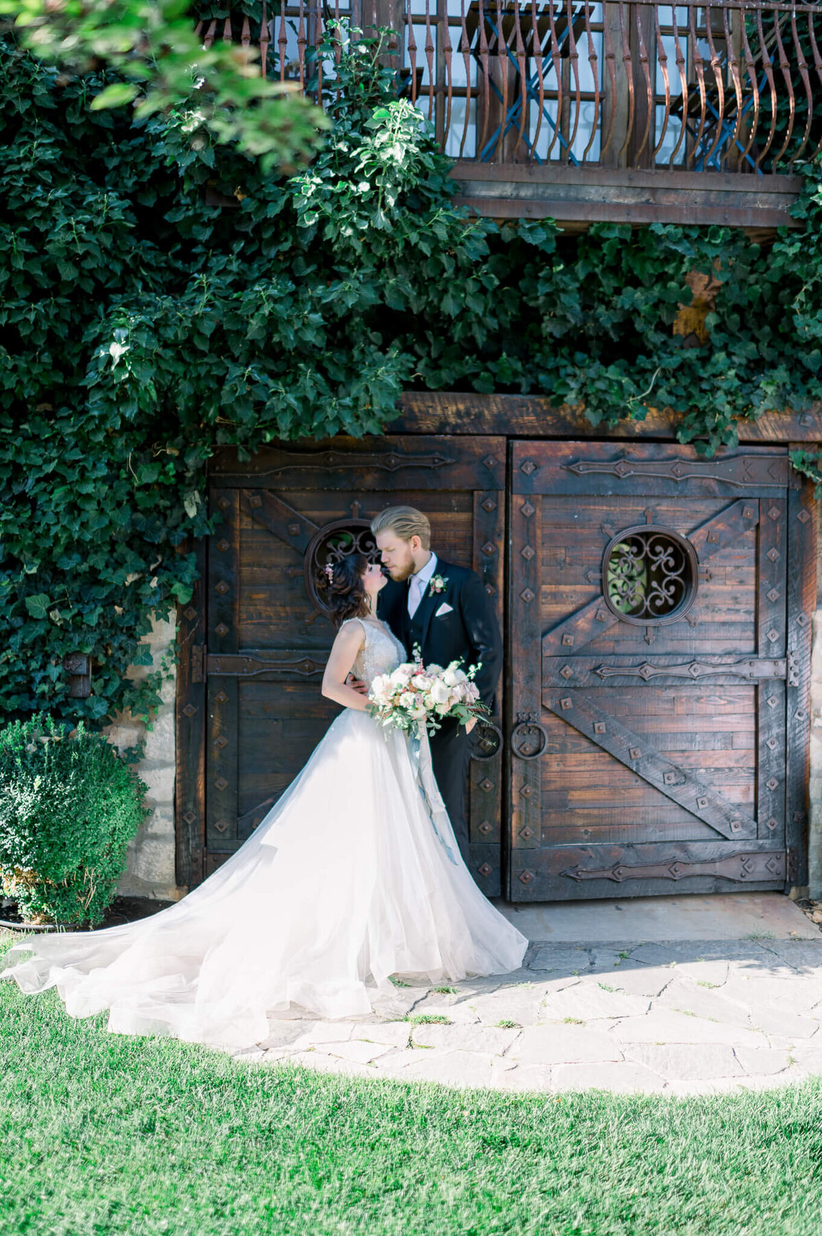 bride and groom pose in wedding attire in front of heavy wooden and metal doors, arkansas wedding photographer