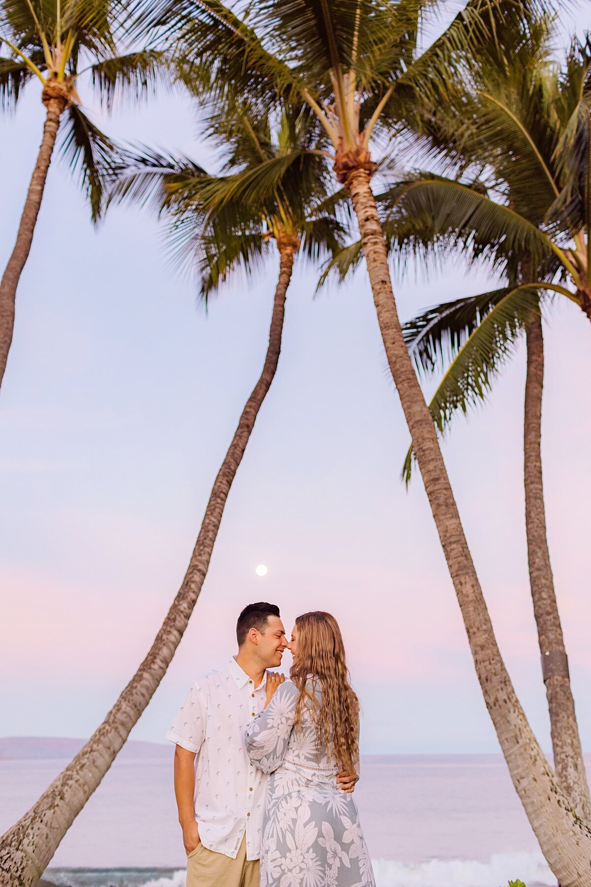 Couple kiss under a full moon in Wailea during their beach portrait session with Love + Water