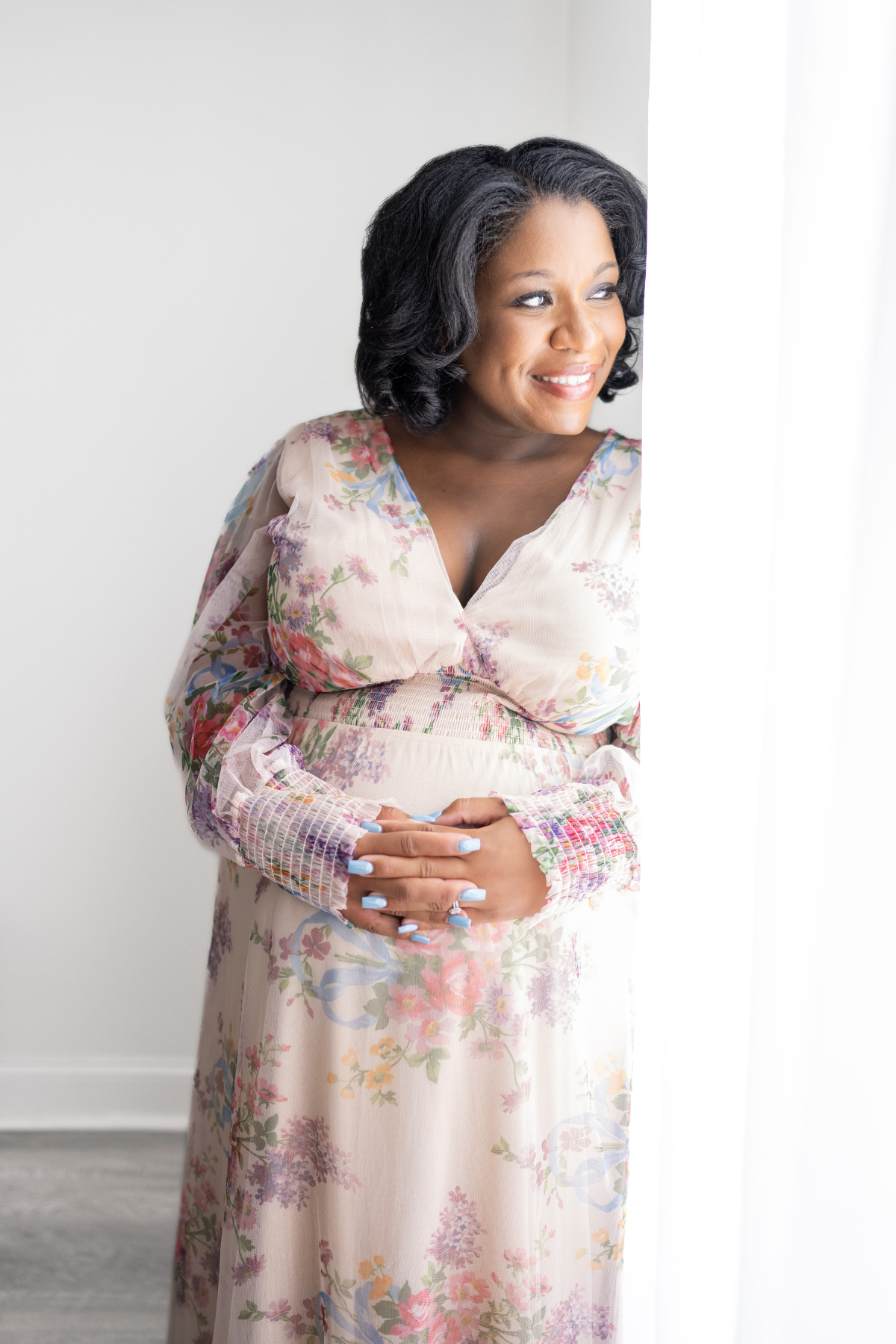 An expectant mother touches her stomach and looks out the window for her maternity pictures
