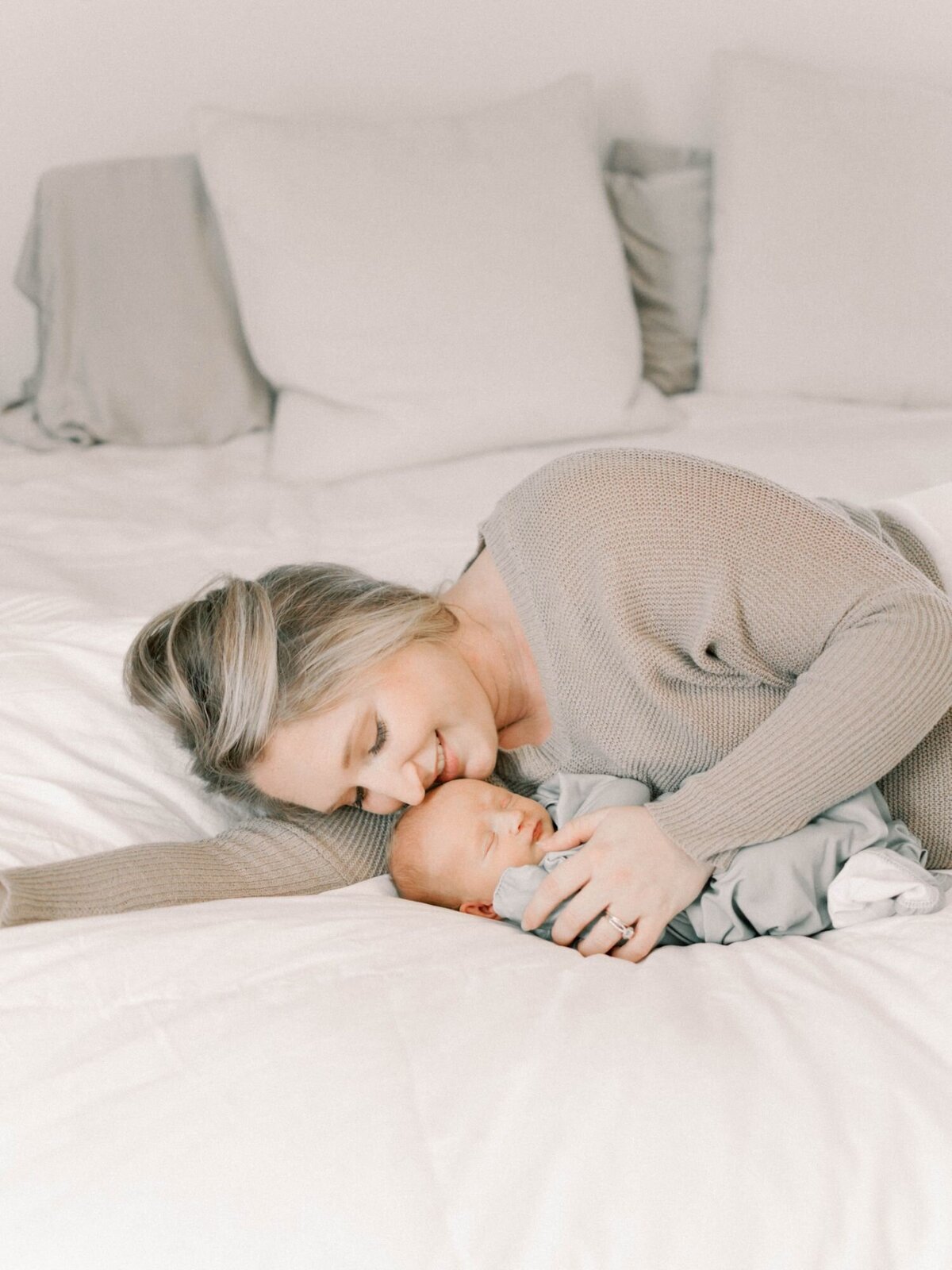 Mother lays on bed kissing newborn baby's forehead.