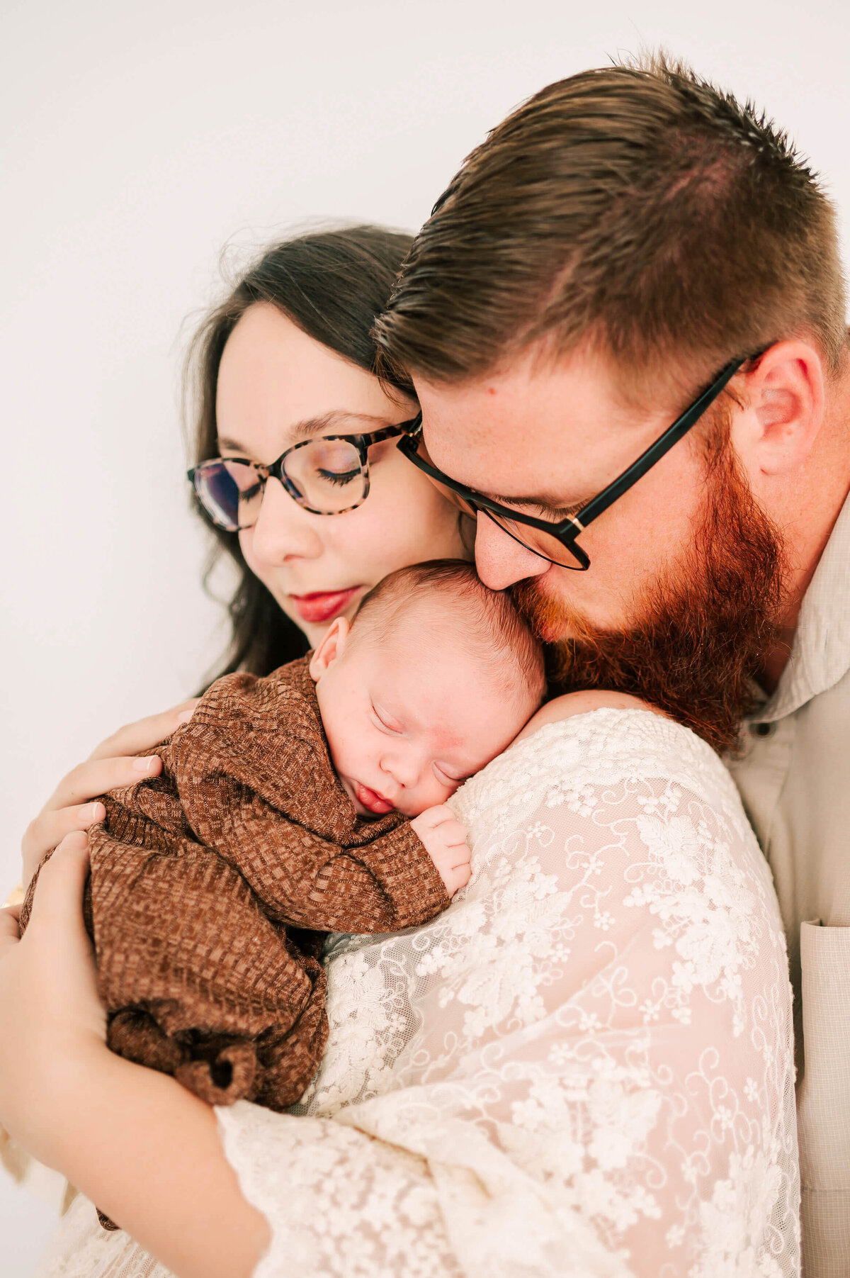 newborn photo in Springfield MO of dad kissing baby on mom shoulder