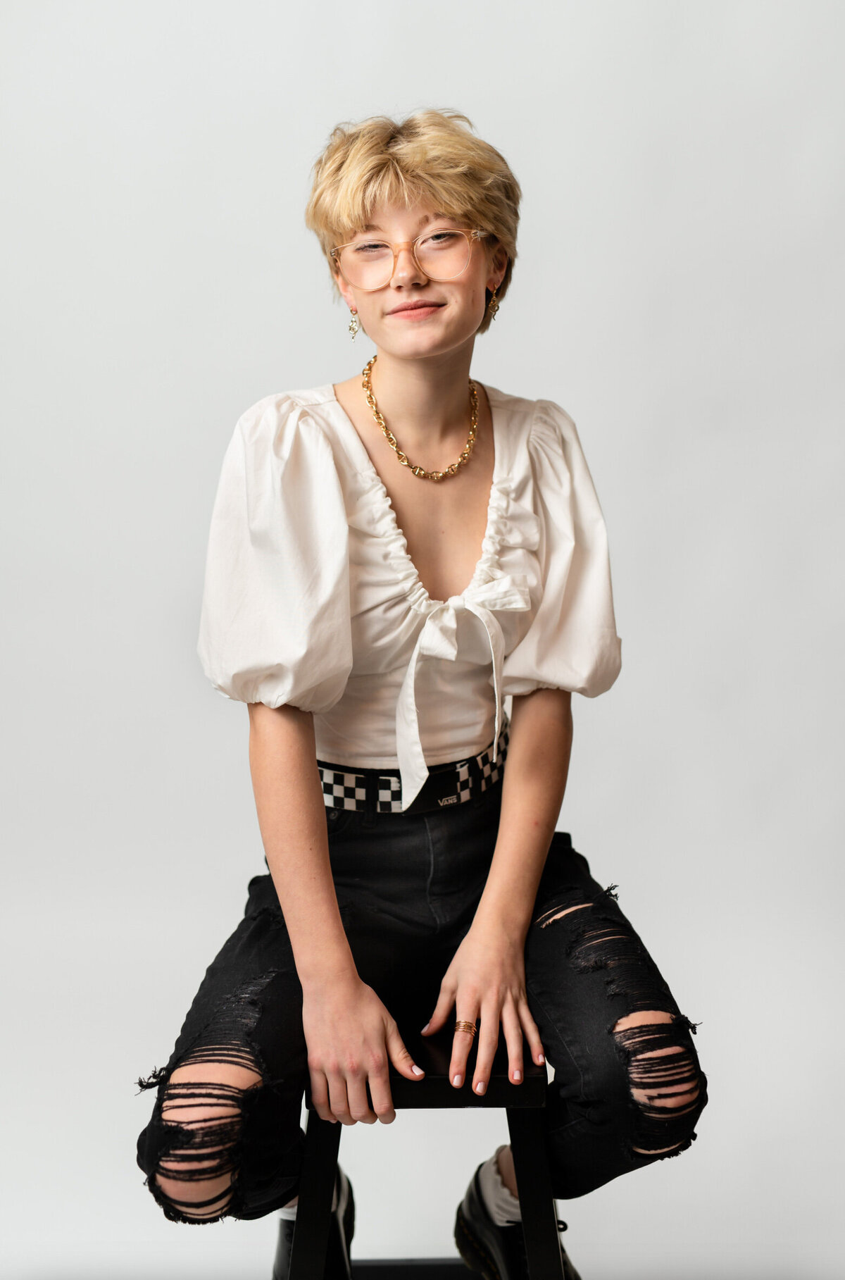 Model posing on a stool wearing black jeans and a white top in front of a white backdrop at a New Jersey headshot studio