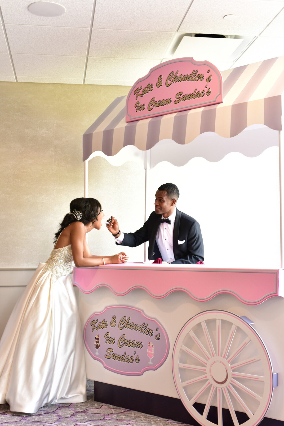 Groom feeding his bride while they both standing and has the dessert cart in between
