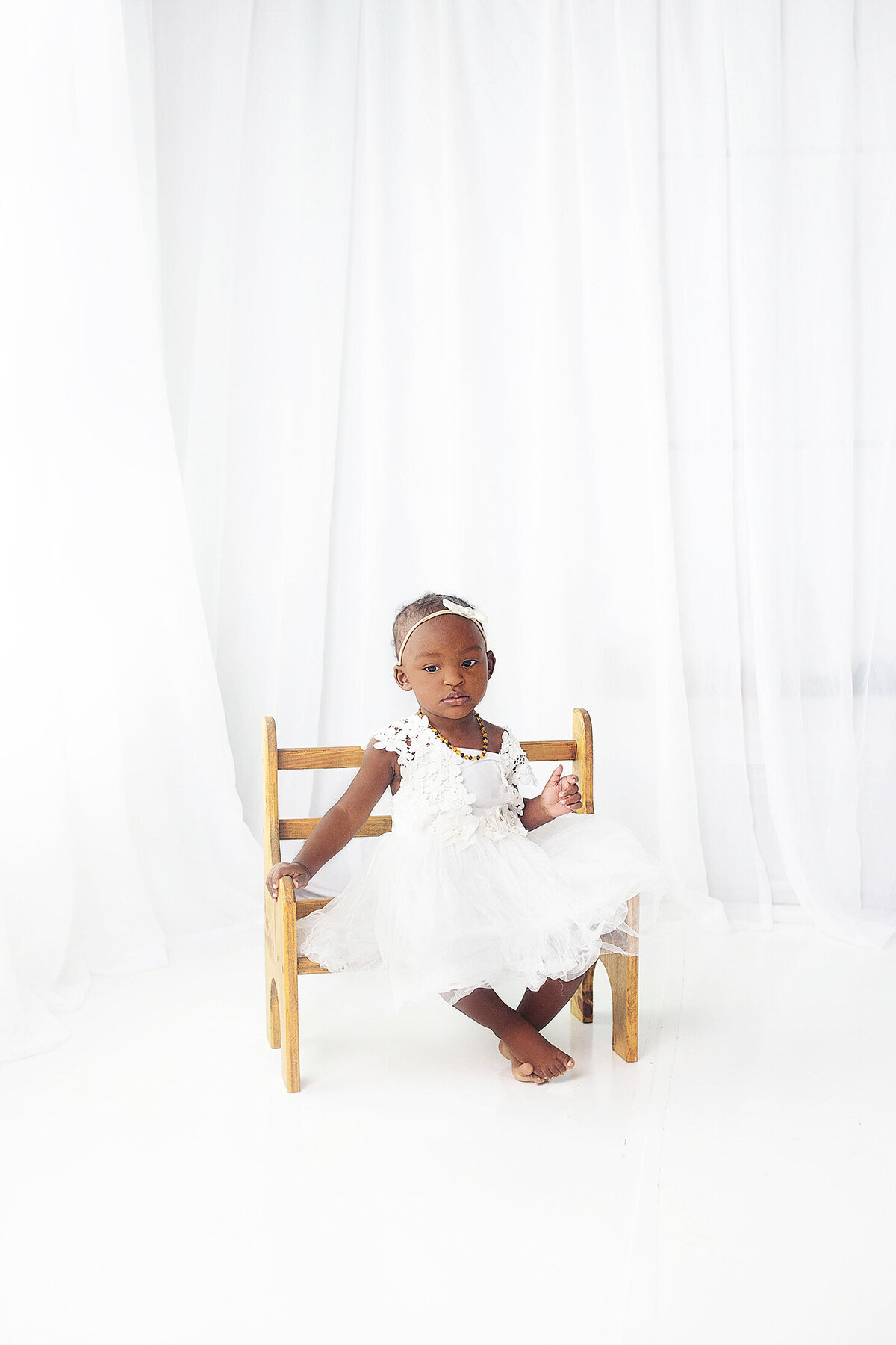 Little girl wearing white, sitting on wood bench during mommy and me photoshoot in  Franklin tennesse photography studio
