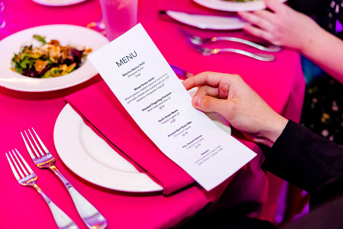 Details of a hand holding a menu on a reception table with pink linen