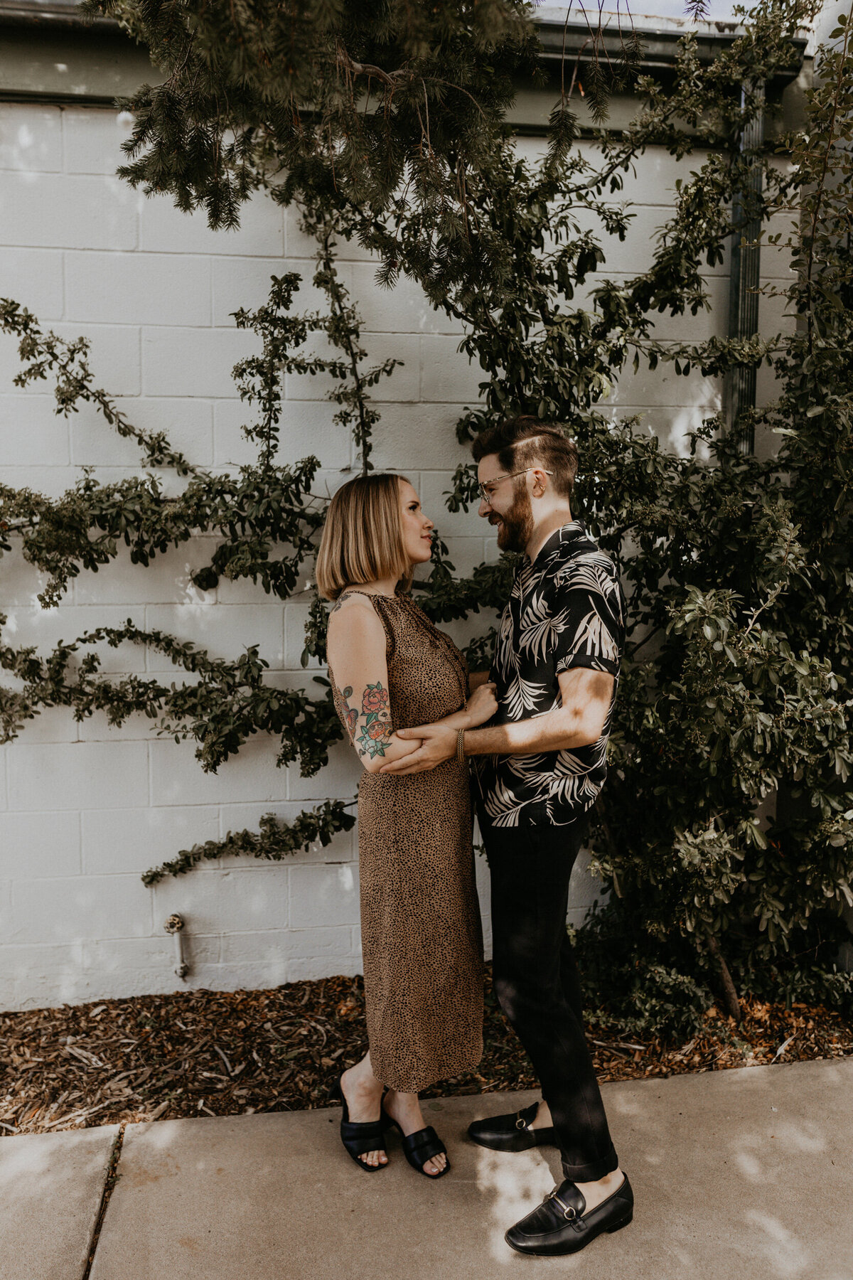 engaged couple looking at each other in front of a vine wall