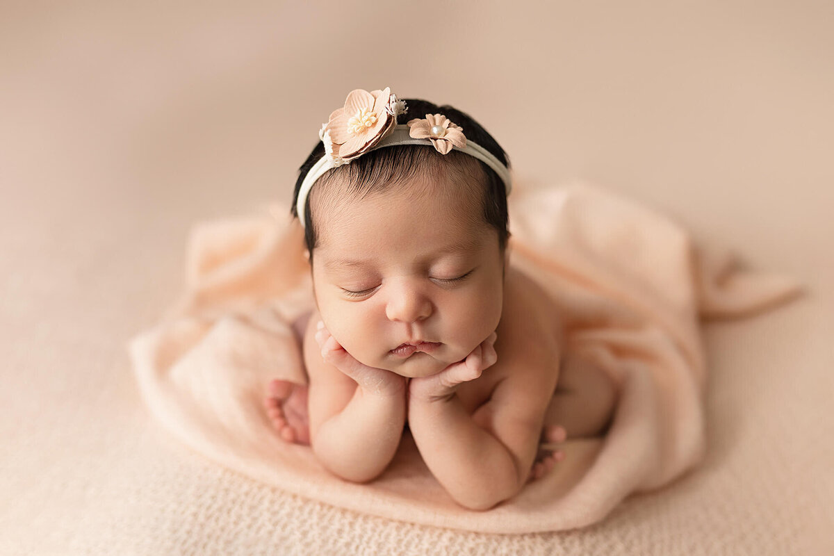Newborn girl posed on light pink fabric during her newborn photo session at Jennifer Brandes Photography.