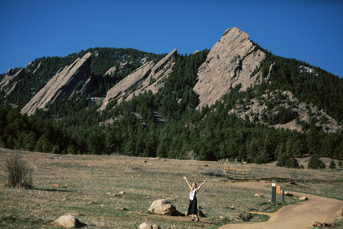 woman raises arms in joy in front of mountains