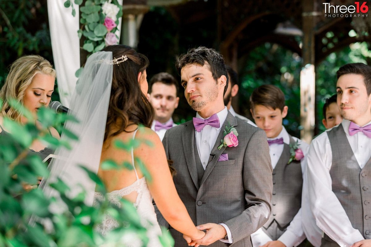 Groom holds his Bride's hand and looks at her during the ceremony as the groomsmen look on