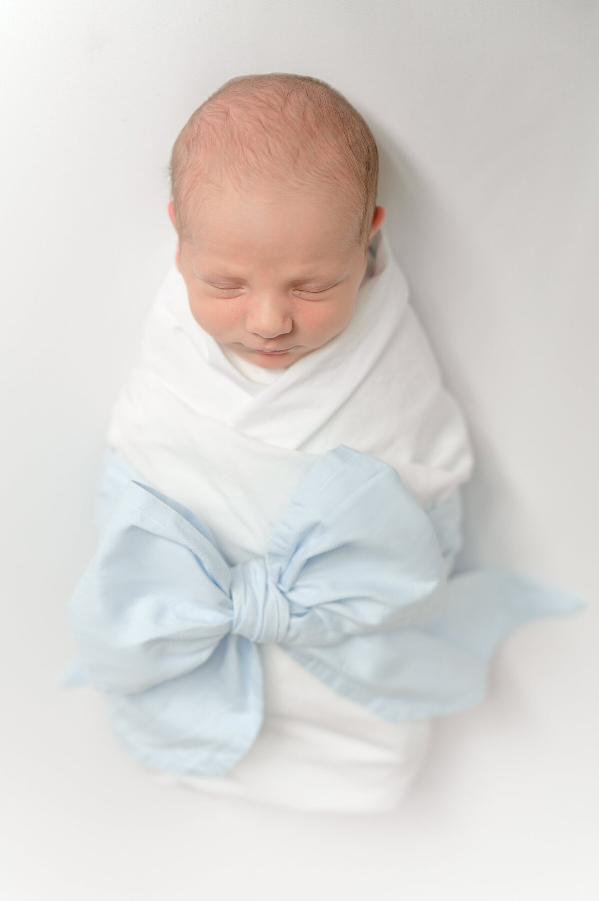 Baby swaddled in a blue bow wrap laying on a white blanket.