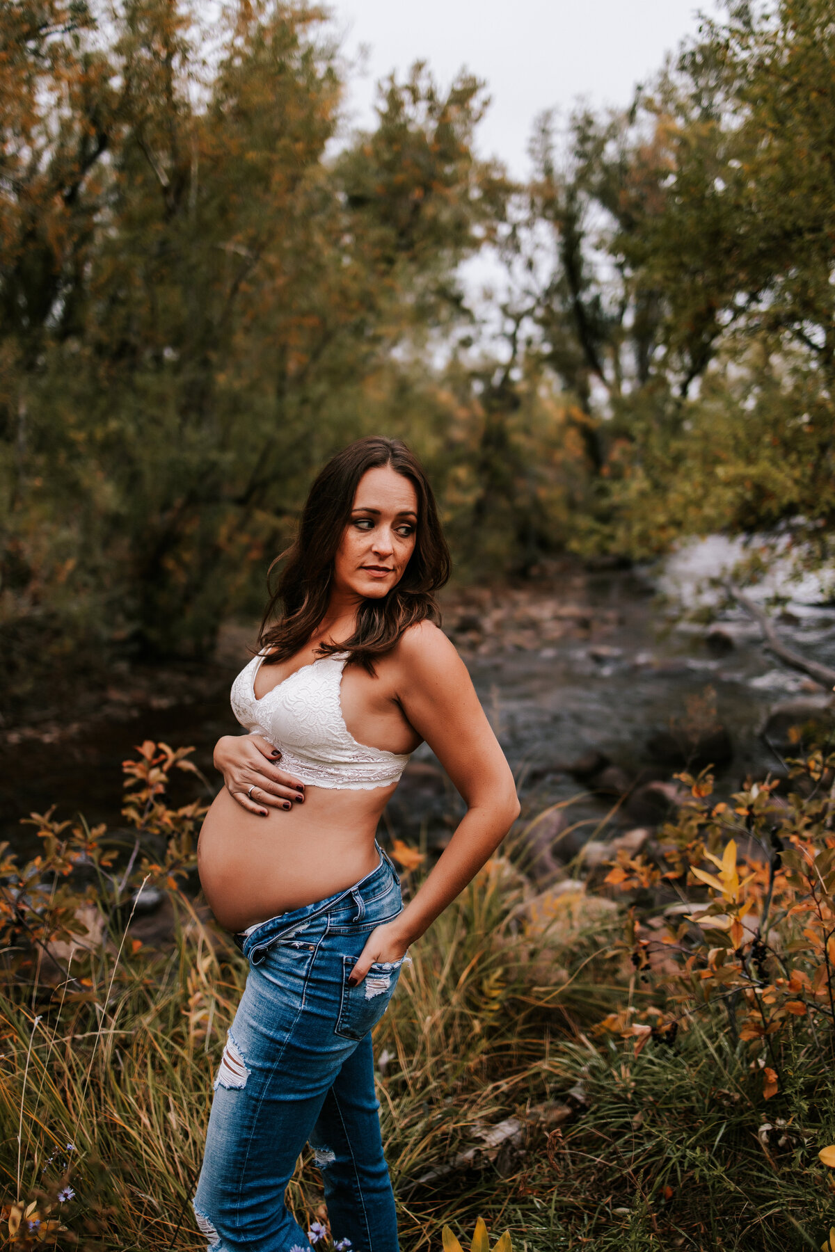 pregnant mom wearing a white bralette and jeans while holding belly in boulder colorado