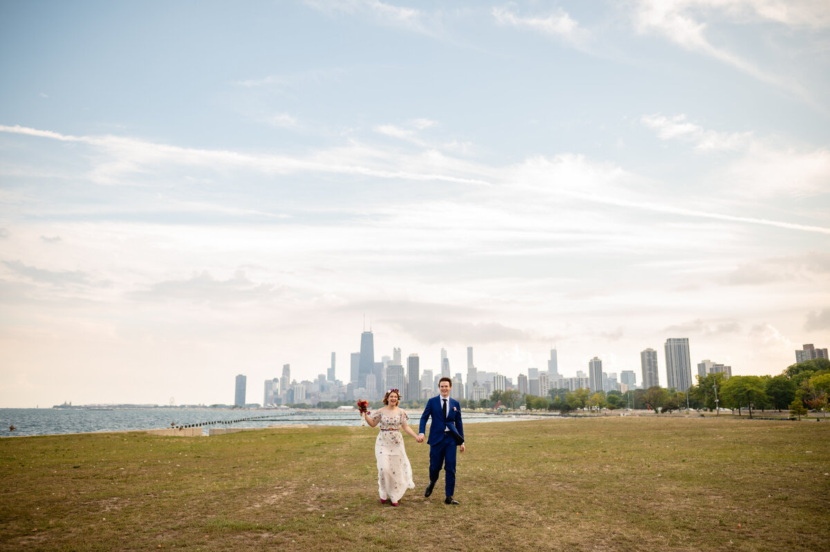 A couple walk in a field with the Chicago skyline in the background