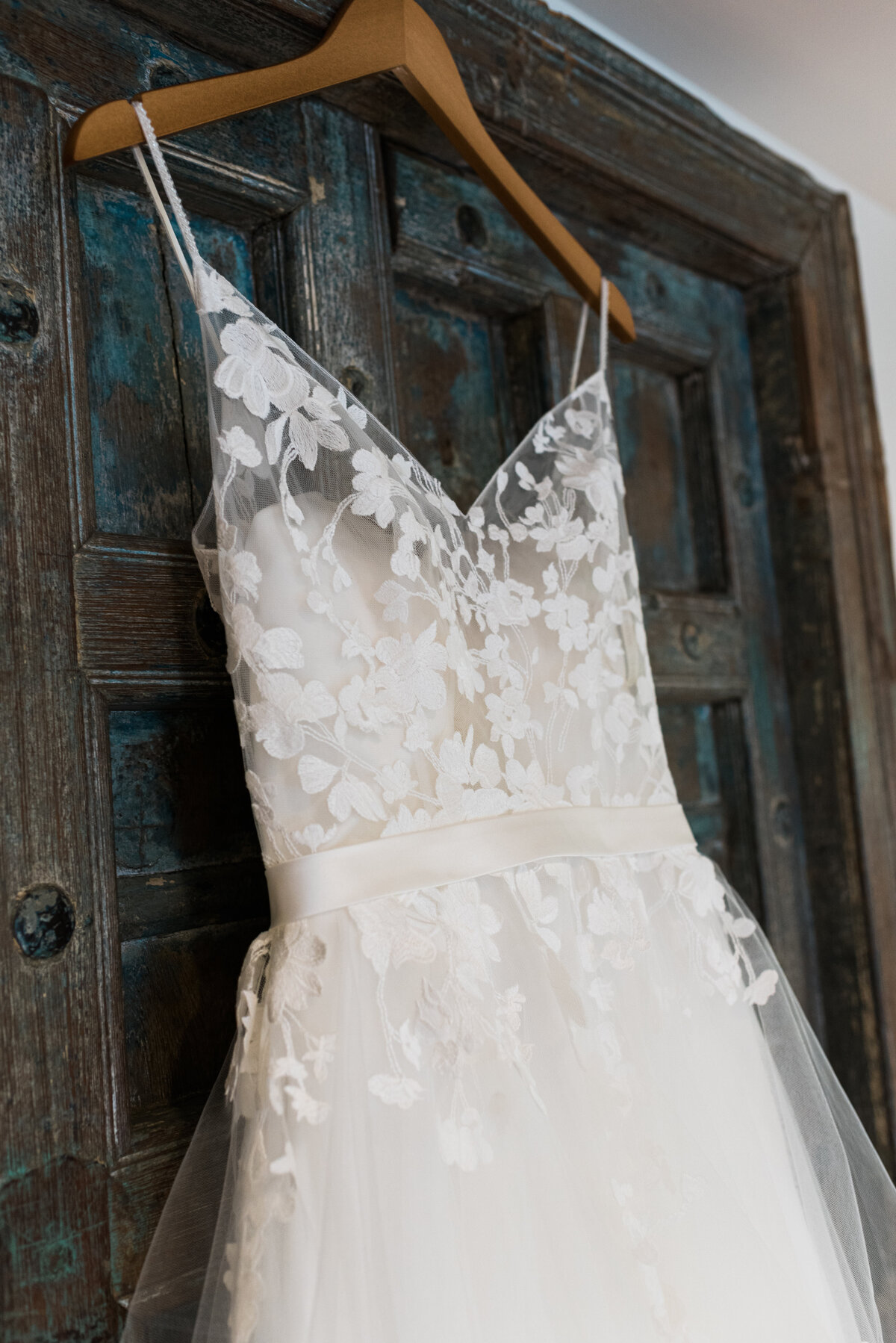 denver wedding photographer photographs detail shot of floral lace wedding dress hanging on a dark blue rustic door of their denver wedding venue's bridal suite