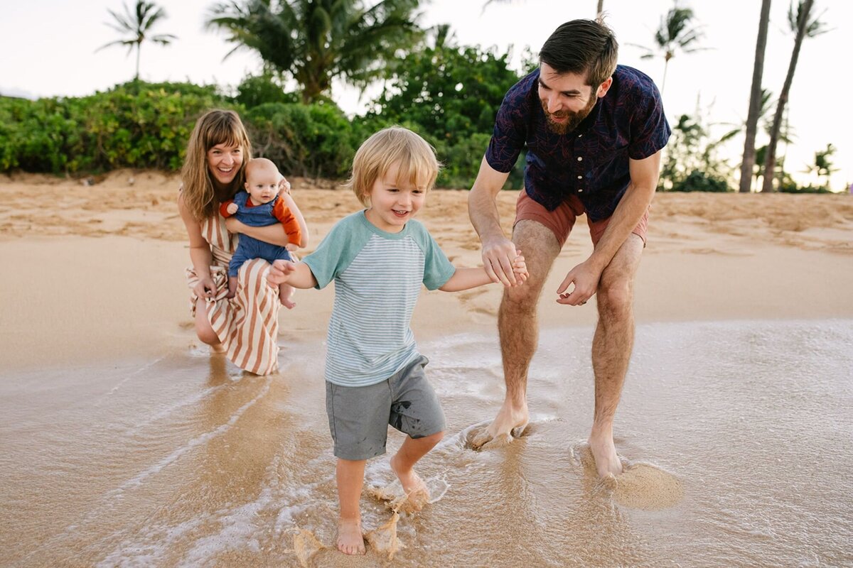 A little boy splashes in the ocean with his parents and infant brother.