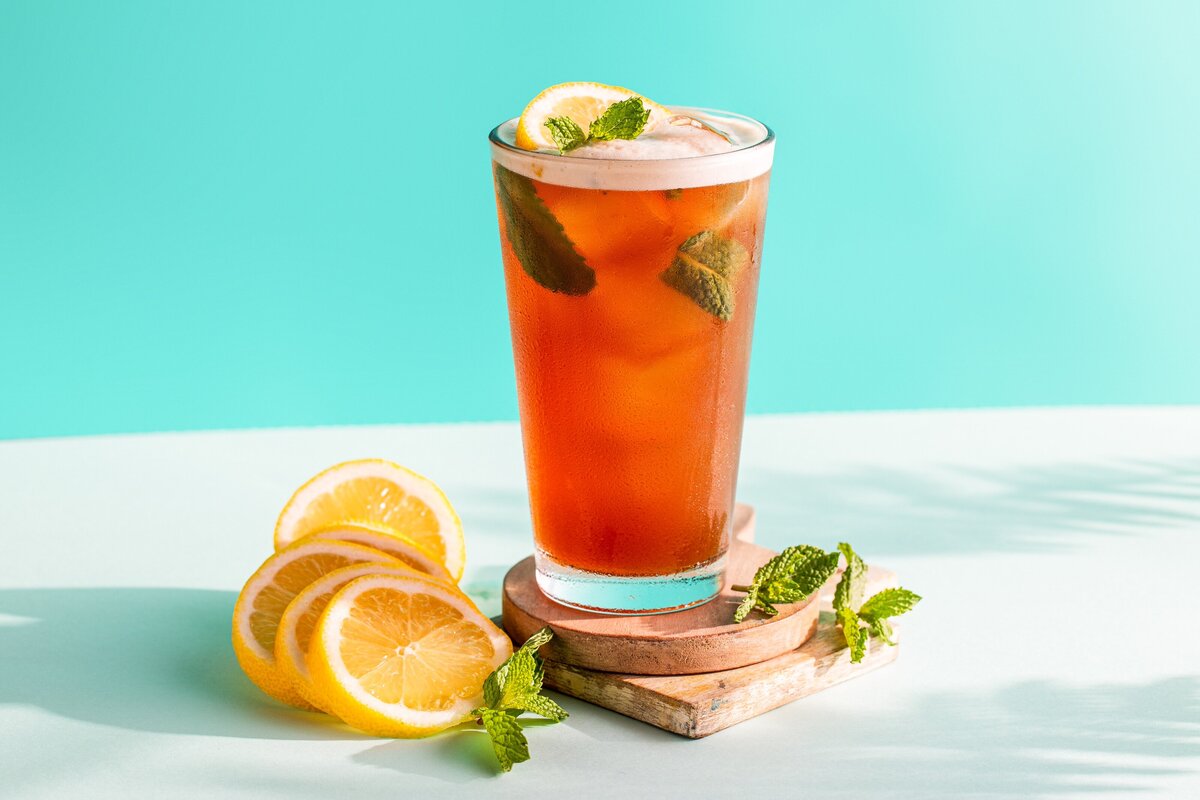 A glass of iced tea with slices of lemon next to it.
