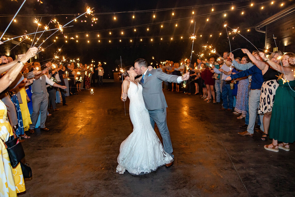 sparkler exit groom kisses bride under string lights Morgan Creek Barn Dripping Springs