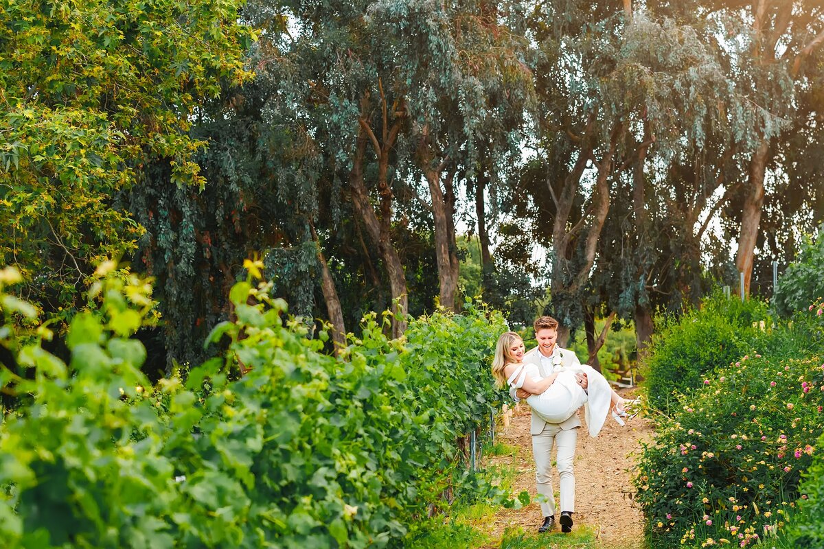 Groom carrying wife through vineyard in Temecula