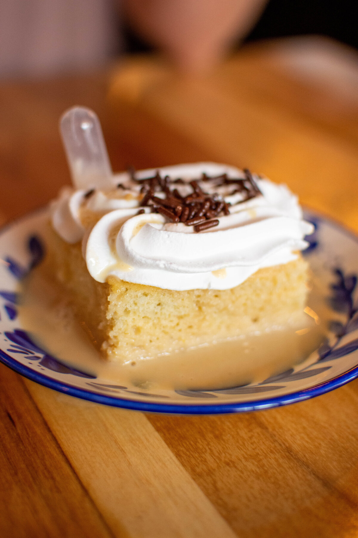 Tres Leches Cake with white frosting and chocolate sprinkles on a blue and white plate