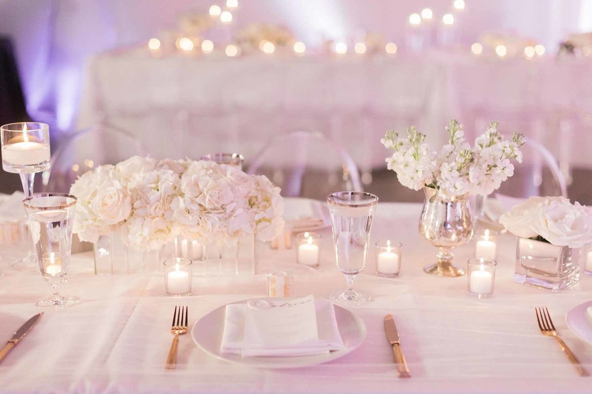 All white candlelit wedding reception table with low arrangements of  stock and hydrangea
