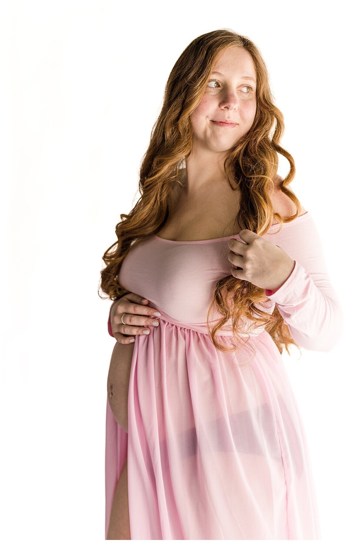 Mom is looking over her shoulder while wearing a beautiful pink dress during a studio Maternity Session in Wexford PA 