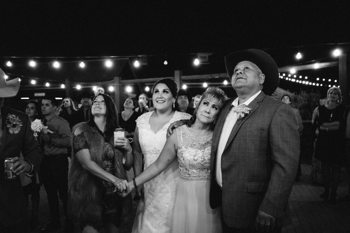 bride looking into sky holding hands with guests for moment of silence at wedding at The Grande Hall at Hoffman Ranch