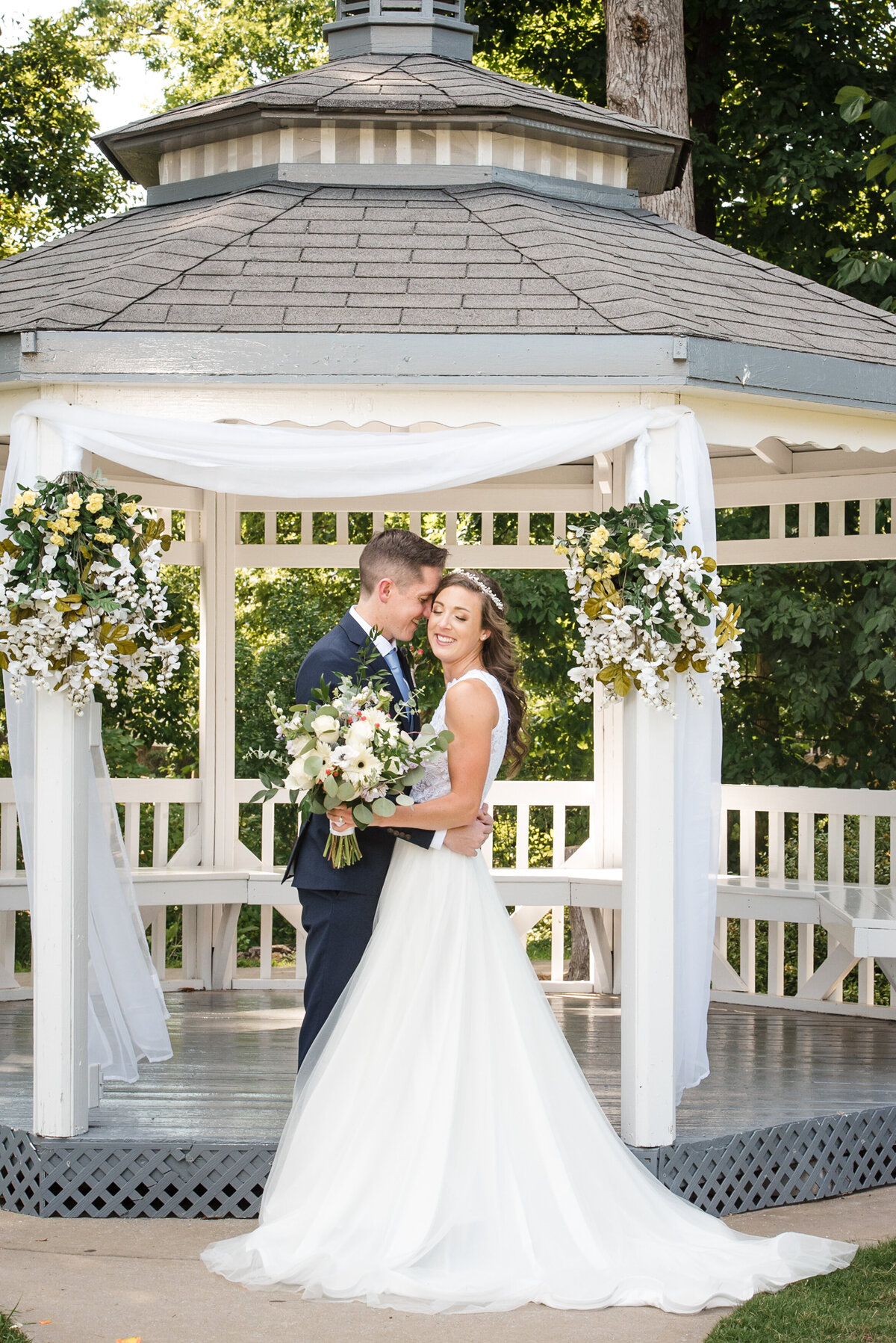 Groom-nuzzling-into-bride's-temple-both-smiling-with-eyes-closed-in-front-of-the-gazebo-at-NorthStone-Country-Club-in-North-Charlotte