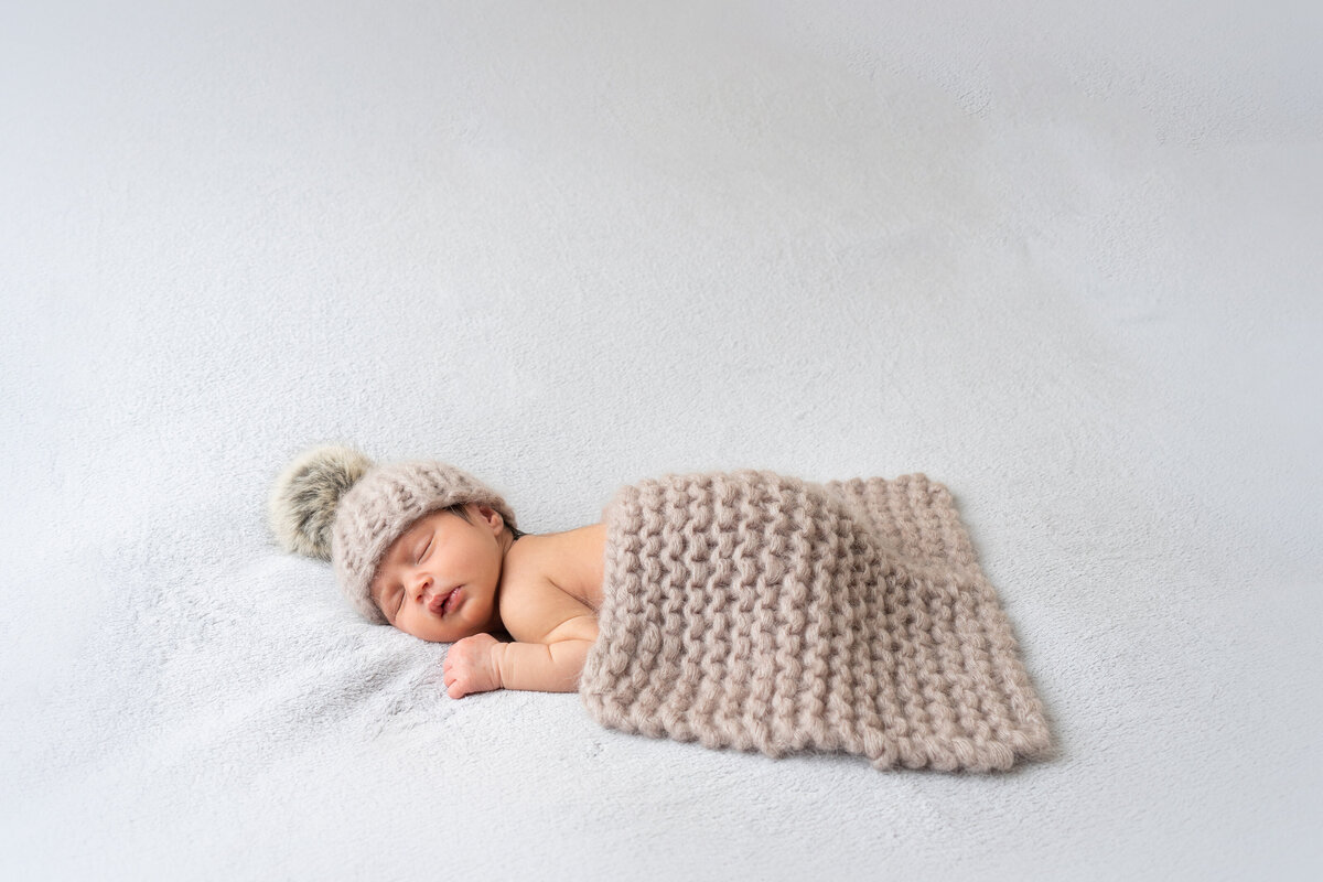 newborn-baby-in-fluffy-hat-posing-on-white-backdrop