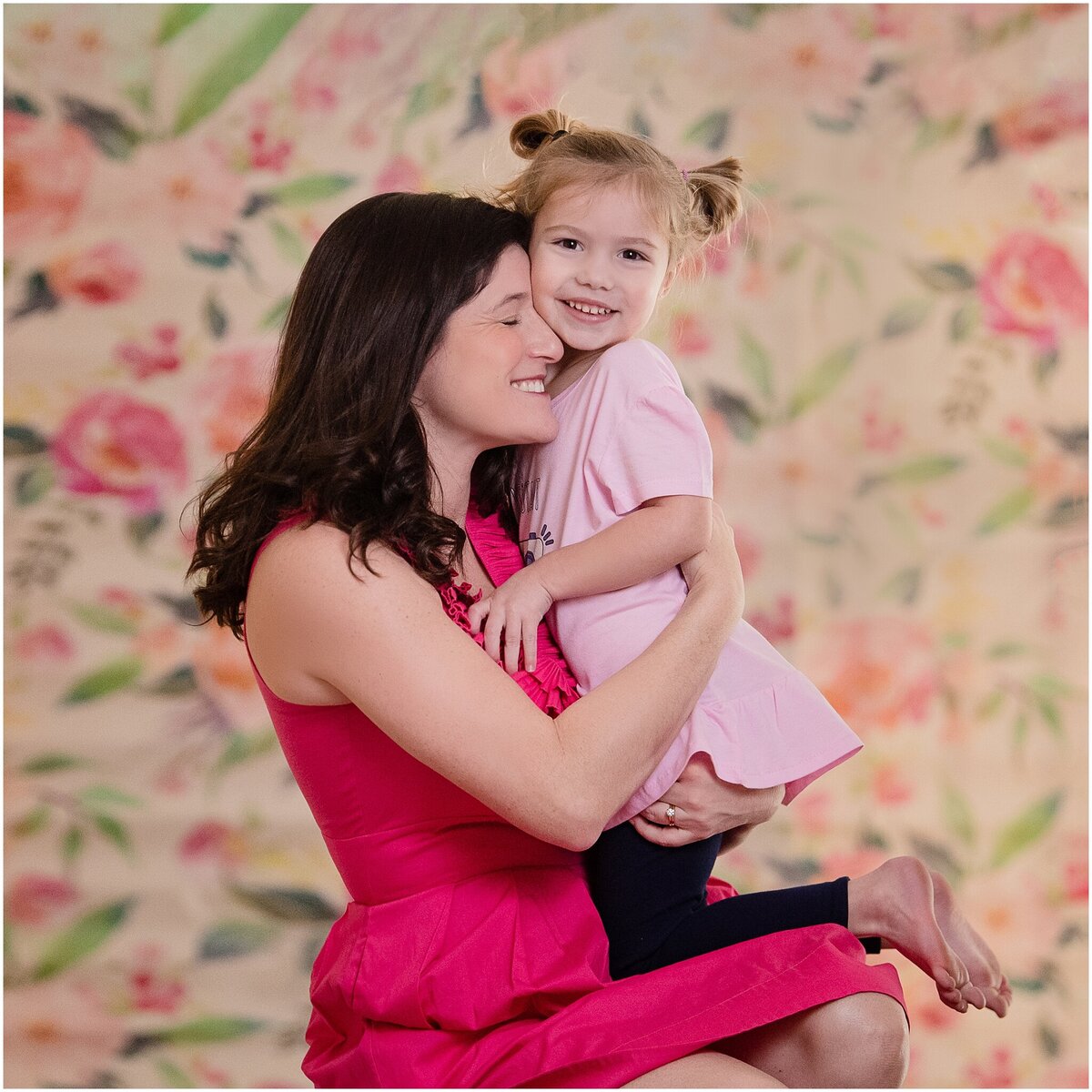 mother and daughter in pink hugging in front of floral backdrop
