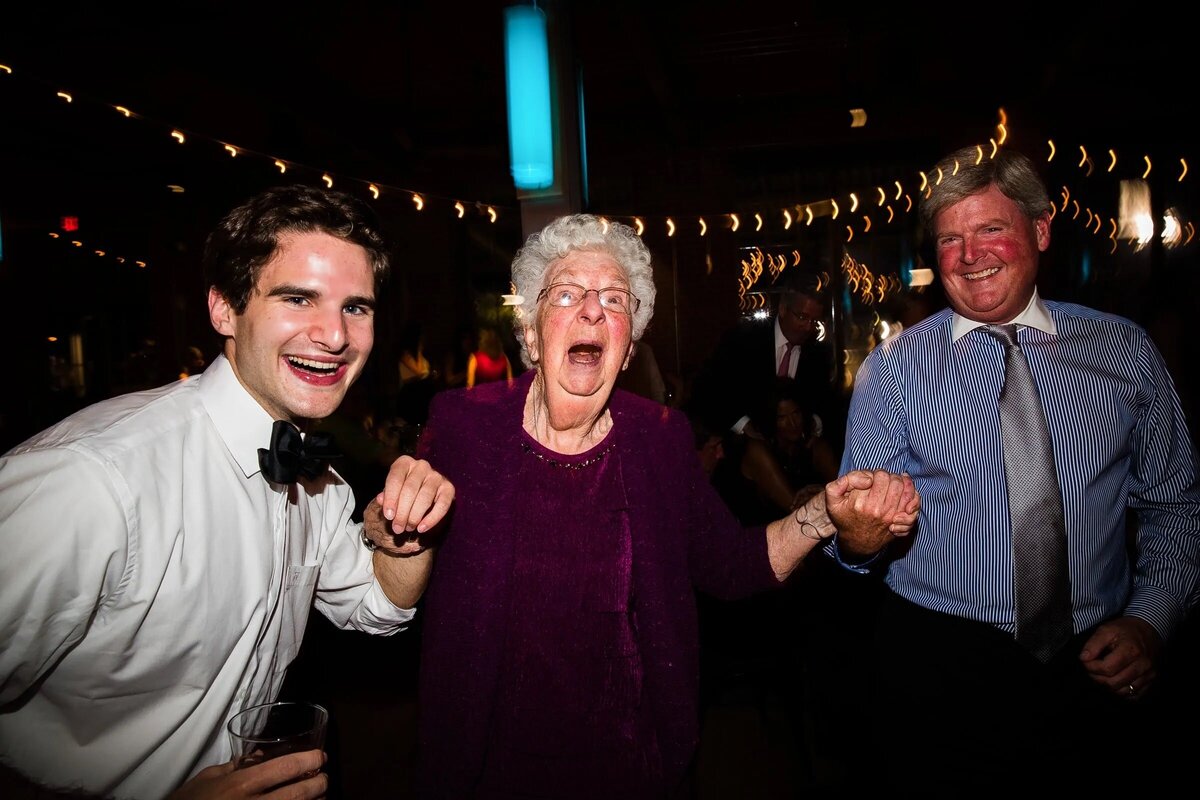 Exuberant dance floor moment with a young man and an elderly woman joyfully dancing together at a wedding reception.