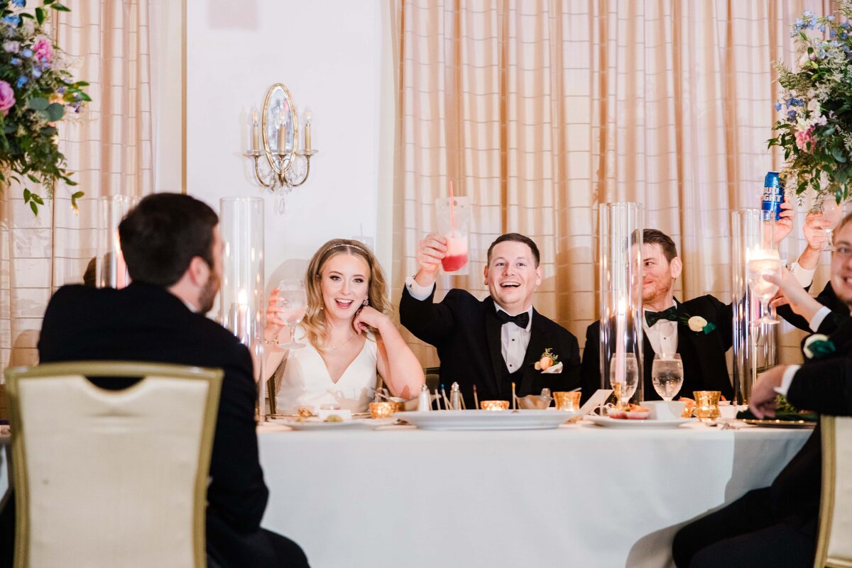 Bride and groom raising toasts at an Iowa wedding reception table, surrounded by guests clinking glasses.