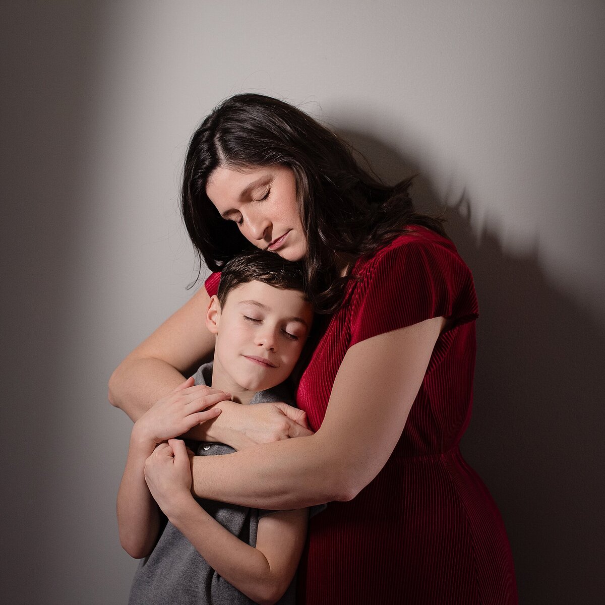 mother in red dress with arms around boy