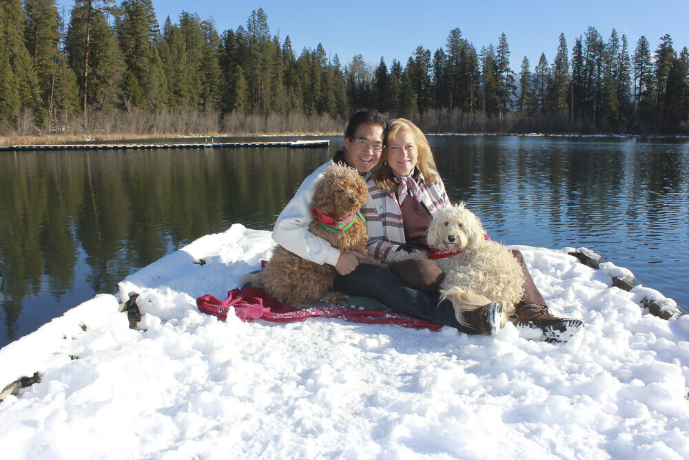 Couple with dogs sitting on a snowy pier on a lake