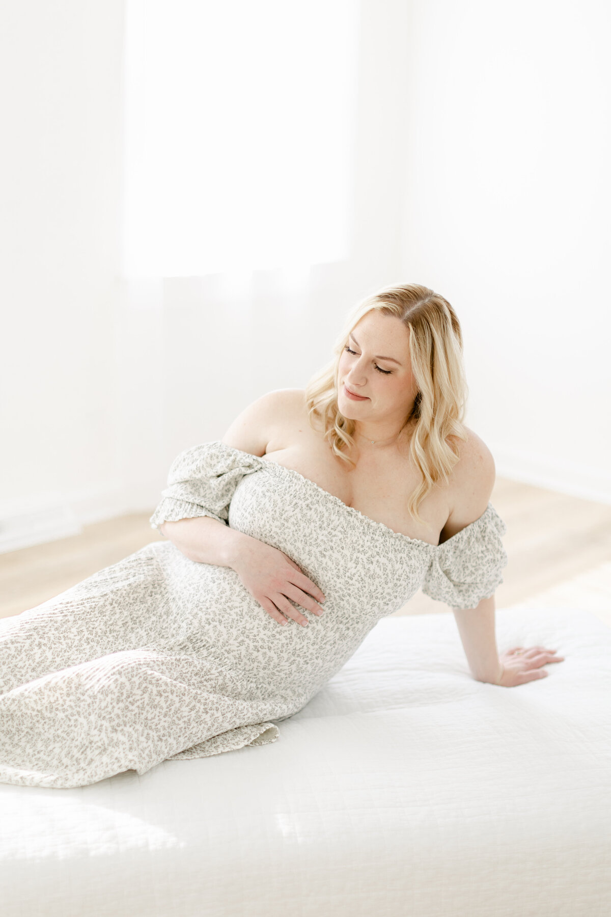 pregnant mom laying on a bed in a bright studio by Philadelphia Maternity Photographer