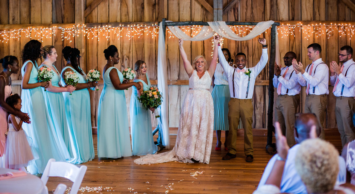 Bride and groom stand with their arms raised at the end of their Betsy's Barn wedding ceremony