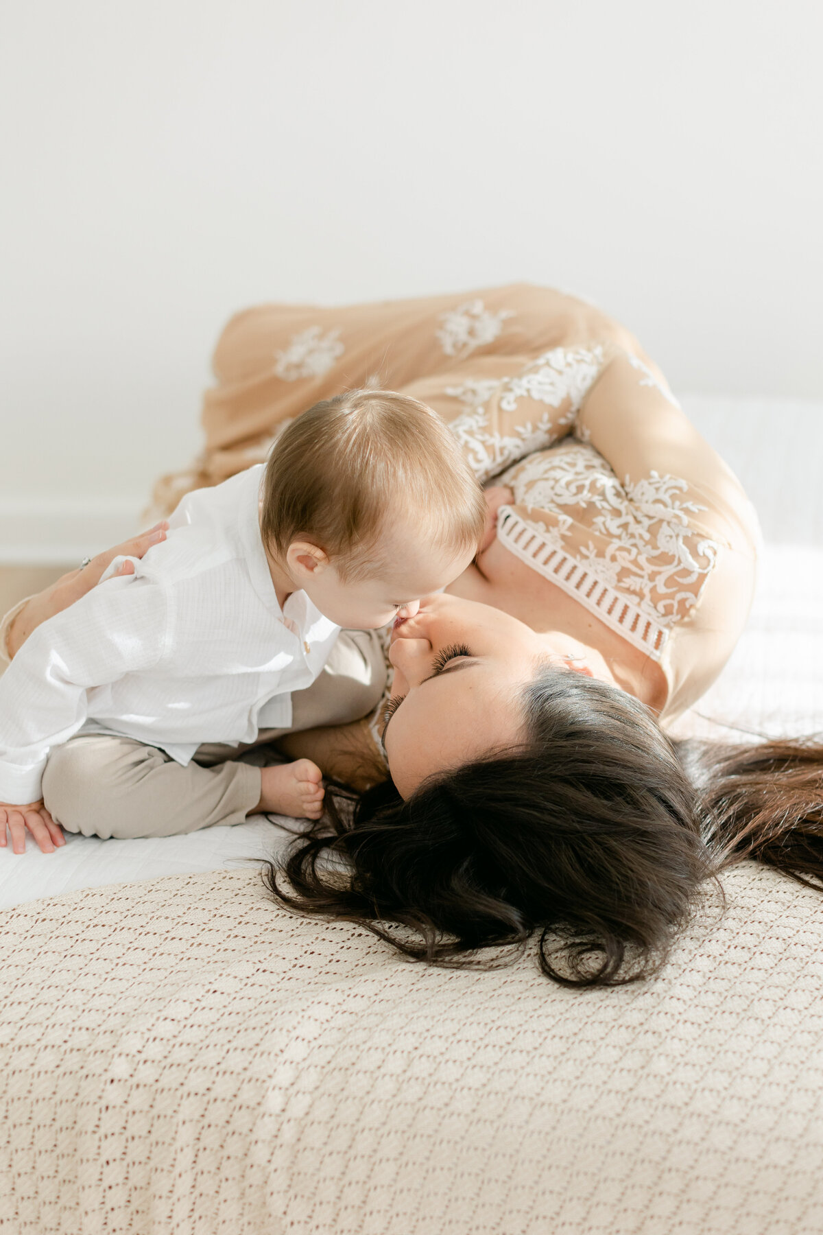 mom kissing her toddler son while laying on a bed in Philadelphia Portrait Photographer Tara Federico's natural light studio