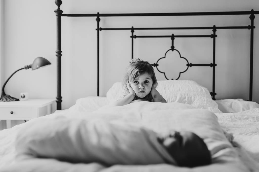Documentary style photo of toddler sibling and newborn on bed in home